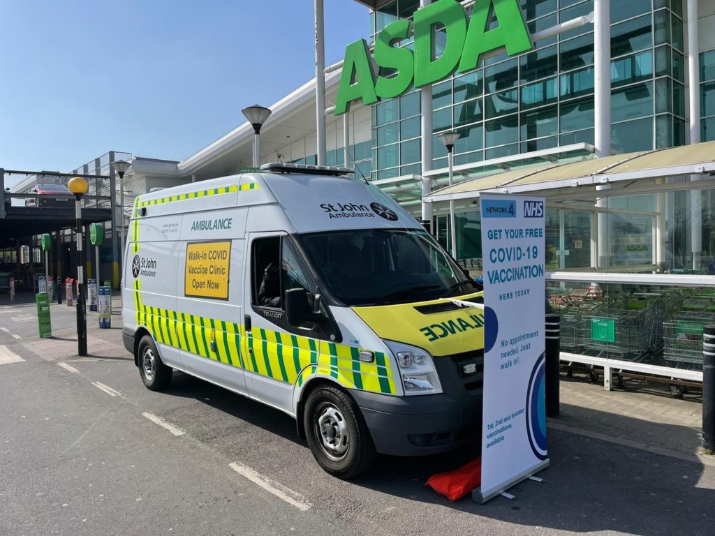 A St. Johns ambulance parked outside an Asda supermarket. There is a sign letting people know that they can get their COVID-19 vaccine there.