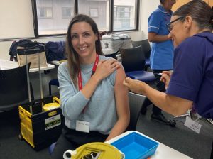 Person smiling at the camera getting vaccinated by a nurse in their left arm.
