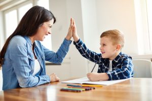 يجلس أحد الوالدين وطفله على طاولة يلونان، ويتبادلان التحية بالأيدي.